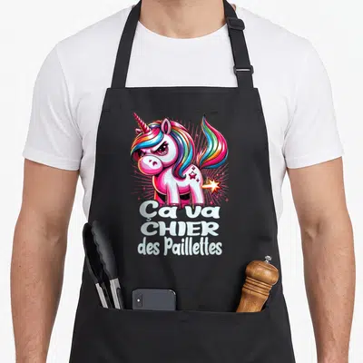 Tablier de cuisine noir avec illustration licorne rose aux cheveux multicolores et texte blanc Ça va chier des paillettes