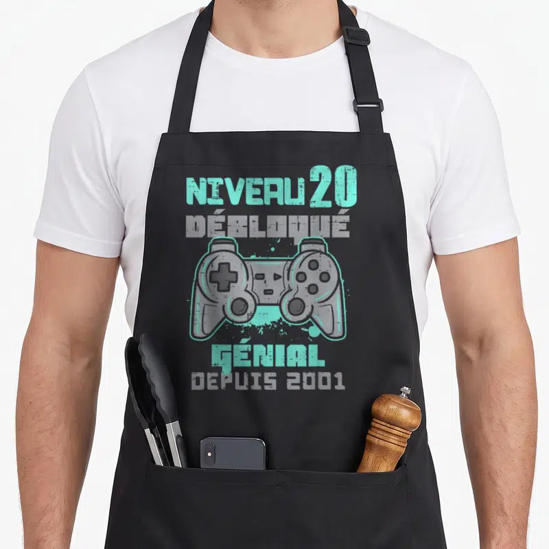 Tablier de cuisine noir avec illustration de manette de jeu vidéo et texte Niveau 20 Débloqué Génial Depuis 2001 en turquoise et gris.