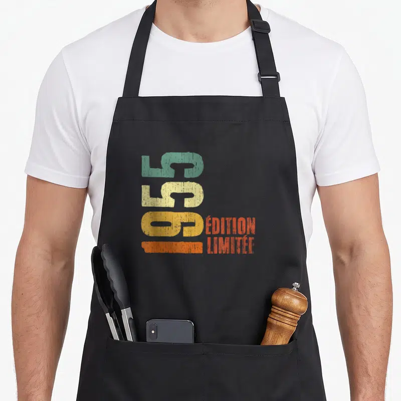 Tablier de cuisine noir avec inscription verticale 70 ans millésime 1955 en couleurs pastel et orange.
