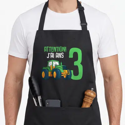 Tablier de cuisine noir avec illustration de tracteur vert, chiffre 3 et texte attention j'ai ans en lettres blanches et vertes.