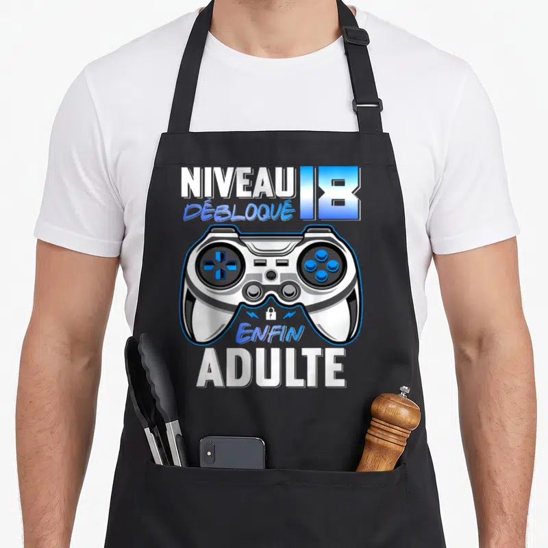 Tablier de cuisine noir avec illustration manette de jeu vidéo et texte Niveau 18 Débloqué Enfin Adulte en blanc et bleu.