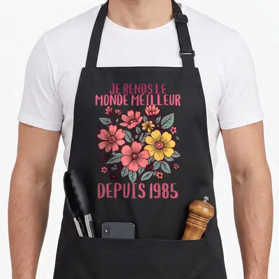 Tablier de cuisine noir avec bouquet de fleurs roses et jaunes et texte Je rends le monde meilleur depuis 1985.