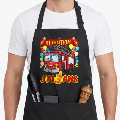 Tablier de cuisine noir avec un camion de pompier rouge souriant, des ballons et le texte Attention j'ai 3 ans.