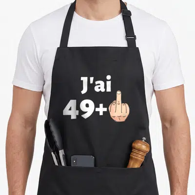 Tablier de cuisine noir avec l'inscription J'ai 49+ et une main gantée montrant le majeur en illustration colorée.