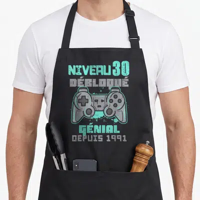 Tablier de cuisine noir avec illustration manette de jeu et texte Niveau 30 Débloqué Génial depuis 1991 en turquoise et gris.