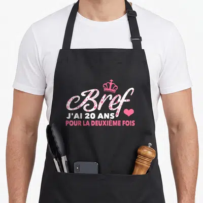 Tablier de cuisine noir avec l'inscription Bref j'ai 20 ans pour la deuxième fois en rose et blanc surmonté d'une couronne.