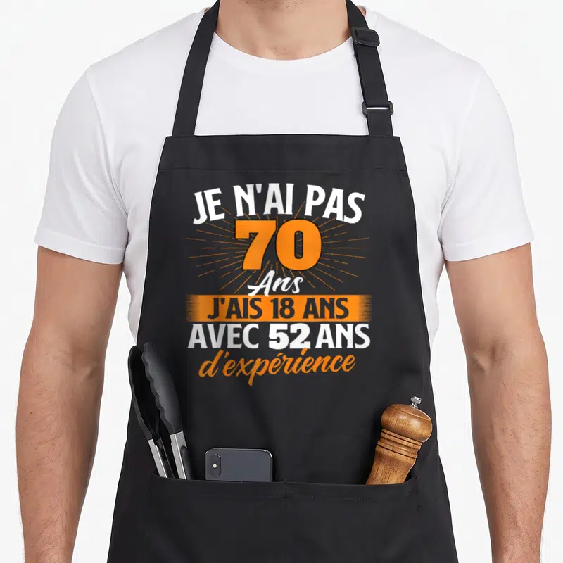 Tablier de cuisine noir avec le texte Je n'ai pas 70 ans j'ais 18 ans avec 52 ans d'expérience en orange et blanc.