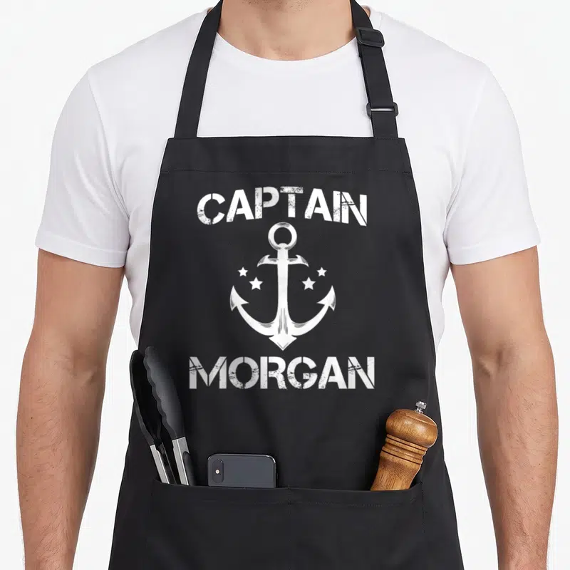 Tablier de cuisine noir avec inscription Captain Morgan et illustration d'ancre blanche entourée d'étoiles.