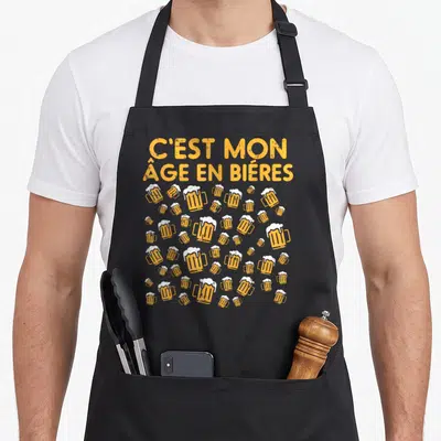 Tablier de cuisine noir avec l'inscription C'est mon âge en bières et des verres d'orange, motif festif.