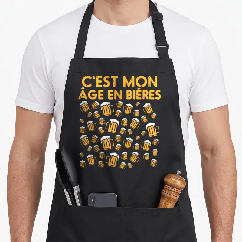 Tablier de cuisine noir avec l'inscription C'est mon âge en bières et des verres d'orange, motif festif.