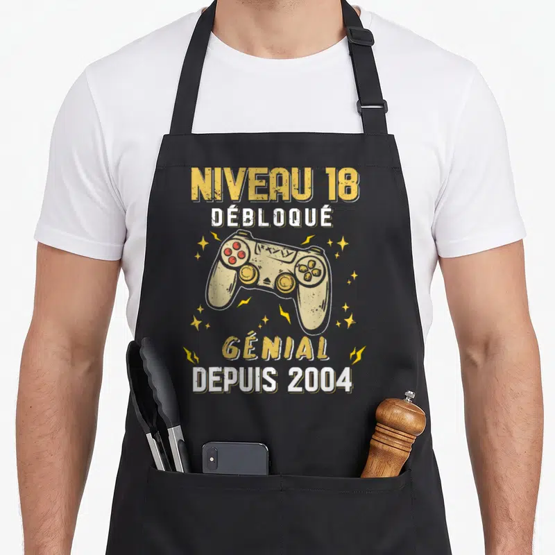 Tablier de cuisine noir avec manette de jeu vidéo et texte Niveau 18 Débloqué Génial Depuis 2004 en jaune et blanc.