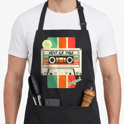 Tablier de cuisine noir avec illustration cassette audio rétro Best of 1982 et accents colorés vintage.
