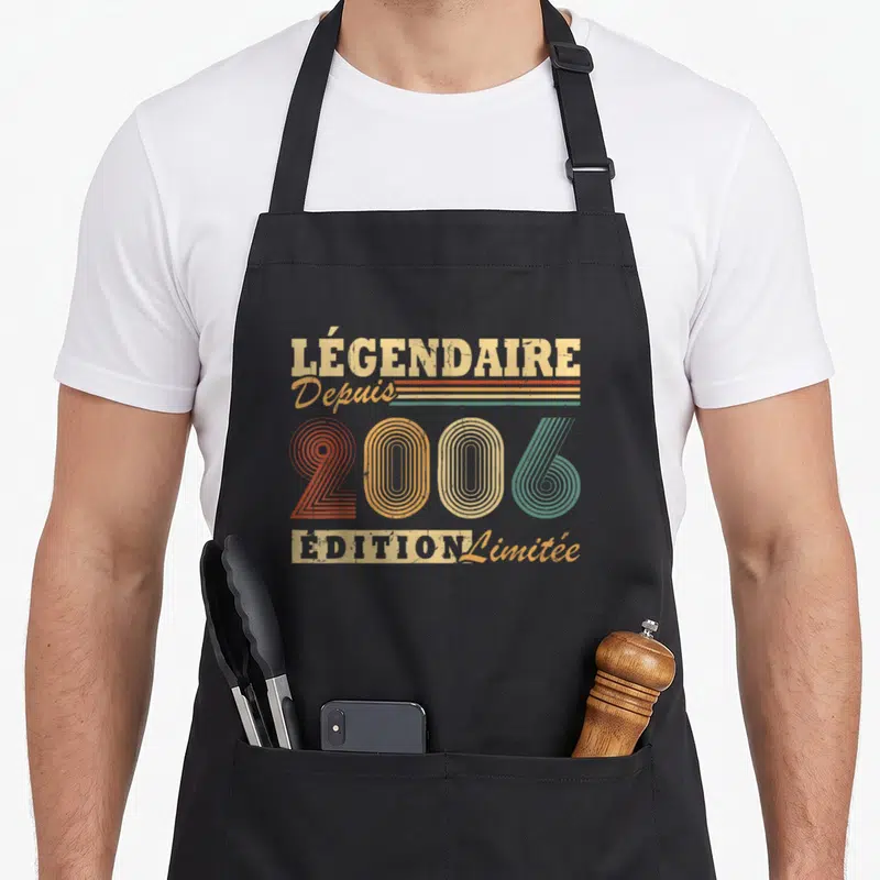 Tablier de cuisine noir avec motif vintage multicolore et texte célébrant une année de naissance spécifique en typographie rétro.