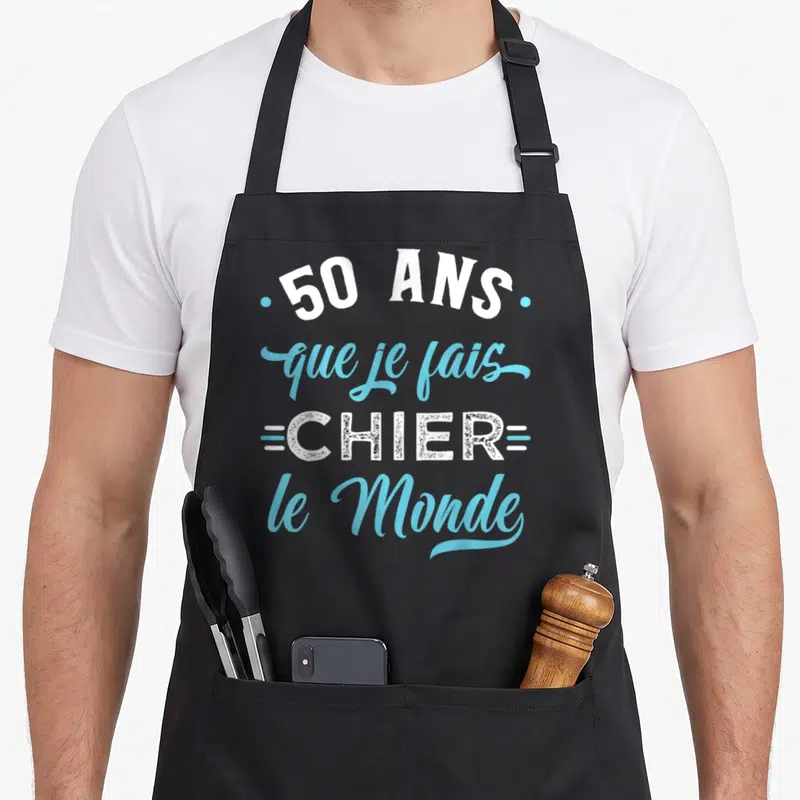 Tablier de cuisine noir avec l'inscription 50 ans que je fais chier le monde en typographie blanche et bleue.