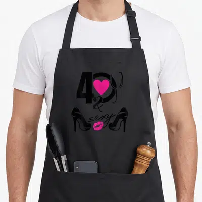 Tablier de cuisine noir avec le chiffre 40, un cœur rose, une coupe de champagne et des talons hauts noirs.