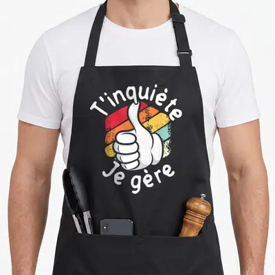 Tablier de cuisine noir avec illustration pouce levé coloré et texte T'inquiète je gère en blanc.
