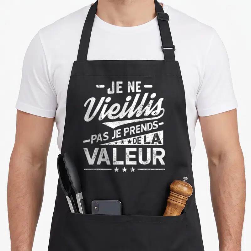 Tablier de cuisine noir avec le texte blanc Je ne vieillis pas je prends de la valeur et des étoiles décoratives.