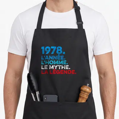 Tablier de cuisine noir avec l'année 1978 et les mots mythe légende imprimés en typographie colorée.