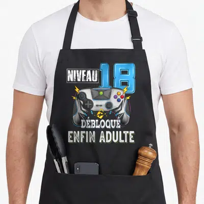 Tablier de cuisine noir avec manette de jeu, éclair et texte Niveau 18 Débloque Enfin Adulte imprimé en couleur.