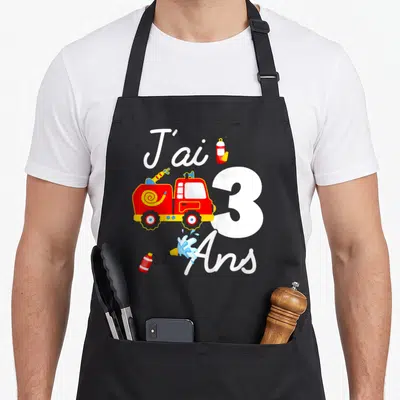 Tablier de cuisine noir avec un camion pompier rouge, le chiffre 3 blanc et des extincteurs colorés.