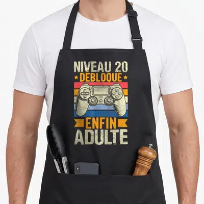 Tablier de cuisine noir avec manette de jeu vidéo et texte Niveau 20 Débloqué Enfin Adulte sur fond coloré vintage.