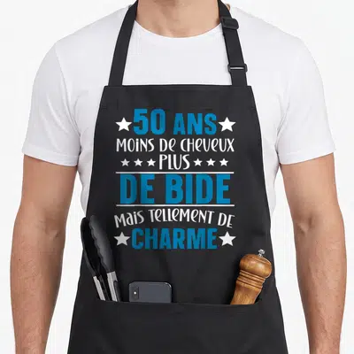 Tablier de cuisine noir avec inscription bleue et blanche 50 ans moins de cheveux plus de bide mais tellement de charme entouré d'étoiles blanches.