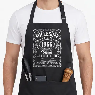 Tablier de cuisine noir avec inscription blanche Millesime 1966 Vieilli à la perfection et cadre floral décoratif.