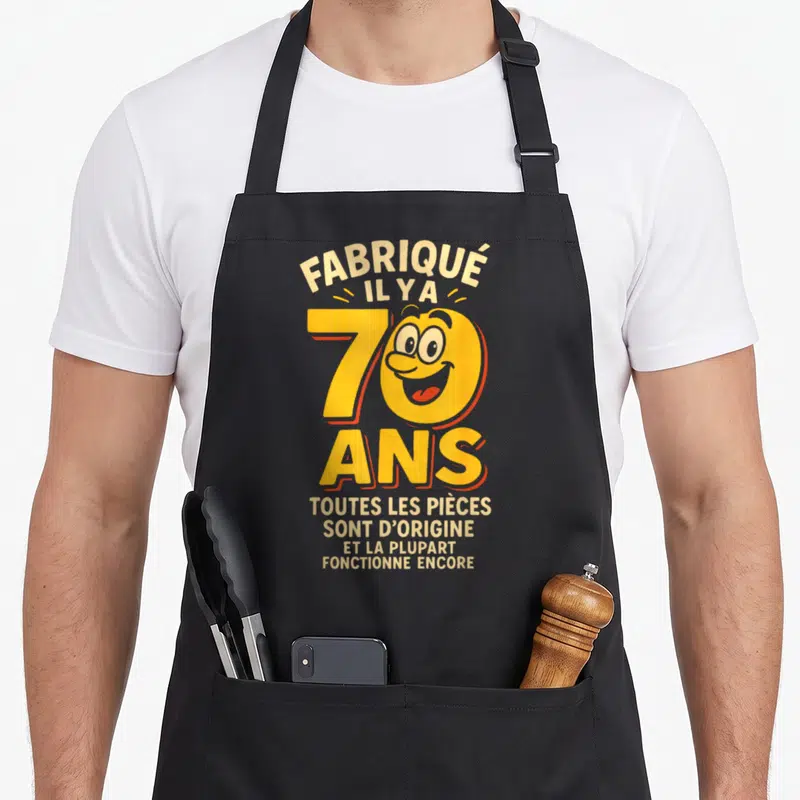 Tablier de cuisine noir avec motif coloré celebrating 70 ans et texte humoristique sur l'âge.