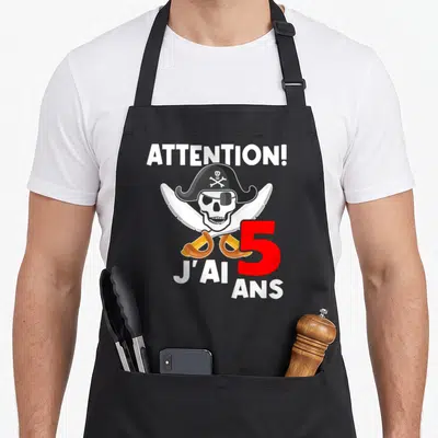 Tablier de cuisine noir avec un crâne de pirate, deux sabres croisés et l'inscription J'ai 5 ans en rouge et blanc.
