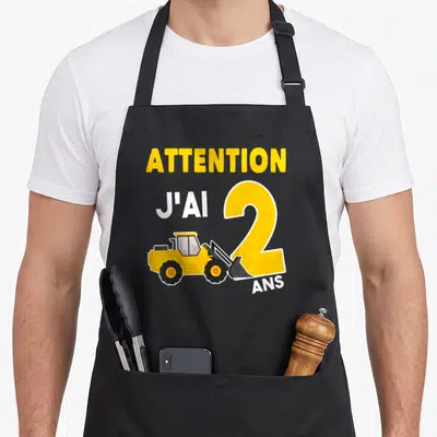 Tablier de cuisine noir avec texte Attention j'ai 2 ans et illustration de bulldozer jaune sur le chiffre deux.
