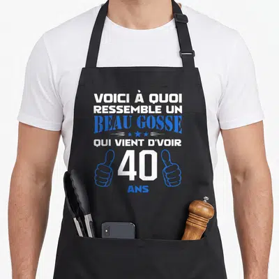 Tablier de cuisine noir avec le texte voici à quoi ressemble un beau gosse qui vient d'avoir 40 ans et deux poignées de main bleues.