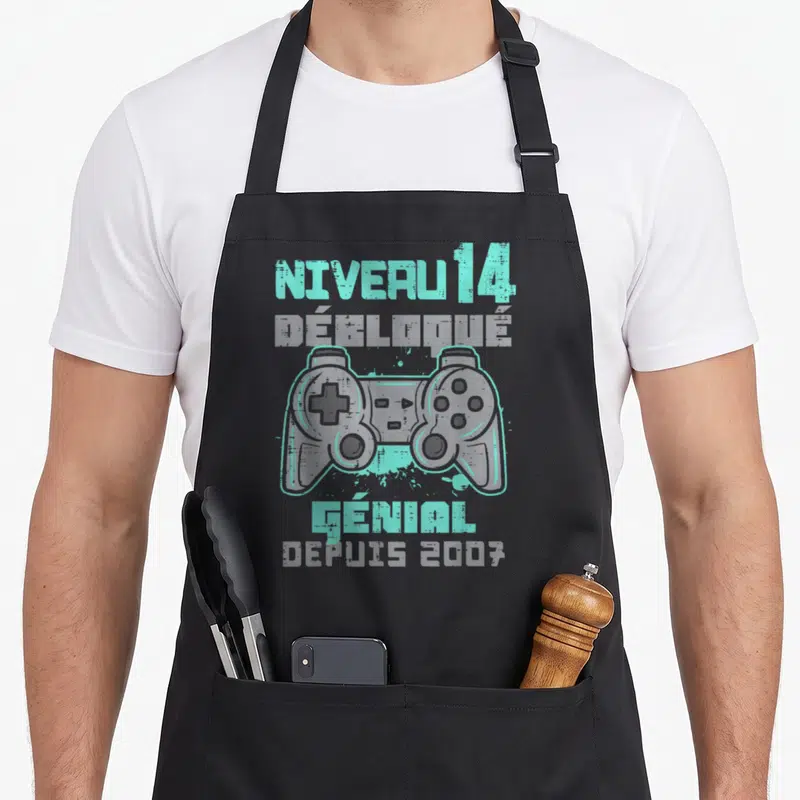 Tablier de cuisine noir avec illustration de manette de jeu vidéo et texte Niveau 14 Débloqué Génial Depuis 2007 en turquoise et gris.