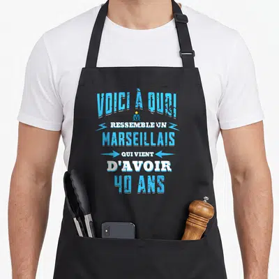 Tablier de cuisine noir avec inscription Voici à quoi ressemble un Marseillais qui vient d'avoir 40 ans en typographie bleue et blanche.