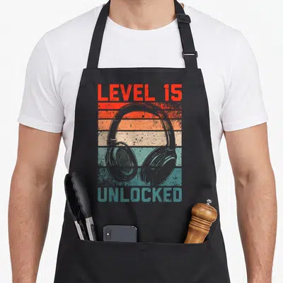 Tablier de cuisine noir avec illustration de casque audio et texte Level 15 Unlocked en style rétro.