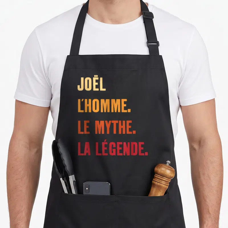 Tablier de cuisine noir avec inscriptionJoël l'homme le mythe la légende en typographie dégradée orange et rouge.