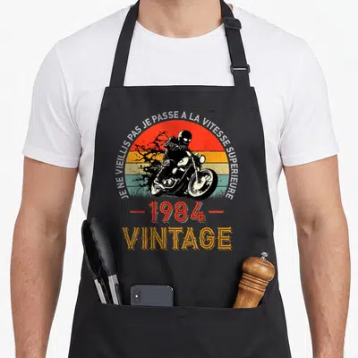 Tablier de cuisine noir avec illustration vintage moto, soleil coloré et texte Je ne vieillis pas je passe à la vitesse superieure.