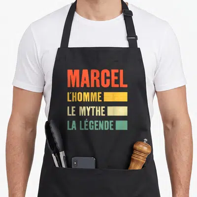 Tablier de cuisine noir avec inscription colorée Marcel l'homme le mythe la légende en lettres capitales stylisées.