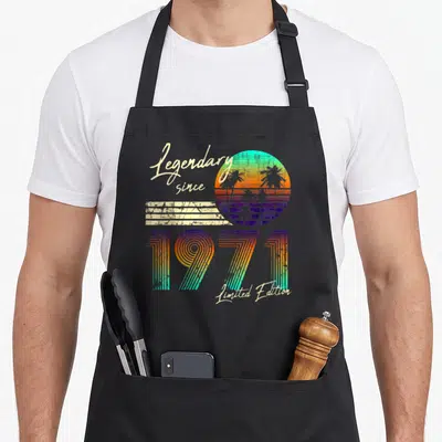 Tablier de cuisine noir avec design rétro 1971, palmiers et texte Legendary since Limited Edition en dégradé coloré.