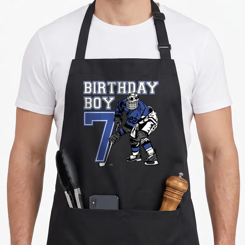 Tablier de cuisine noir avec illustration d'un joueur de hockey et l'inscription anniversaire Boy 7 ans en bleu et blanc.