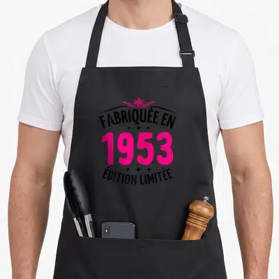 Tablier de cuisine noir avec l'inscription Fabriquée en 1953 « Édition Limitée » en rose vif et une petite couronne stylisée.