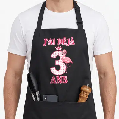 Tablier de cuisine noir avec l'inscription J'ai déjà 3 ans, un flamant rose et une couronne de princesse rose à pois blancs.