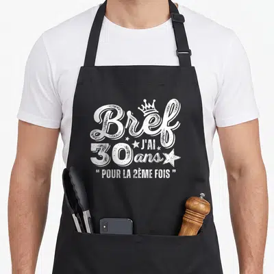 Tablier de cuisine noir avec l'inscription blanche Brief j'ai 30 ans pour la 2ème fois et une petite couronne.
