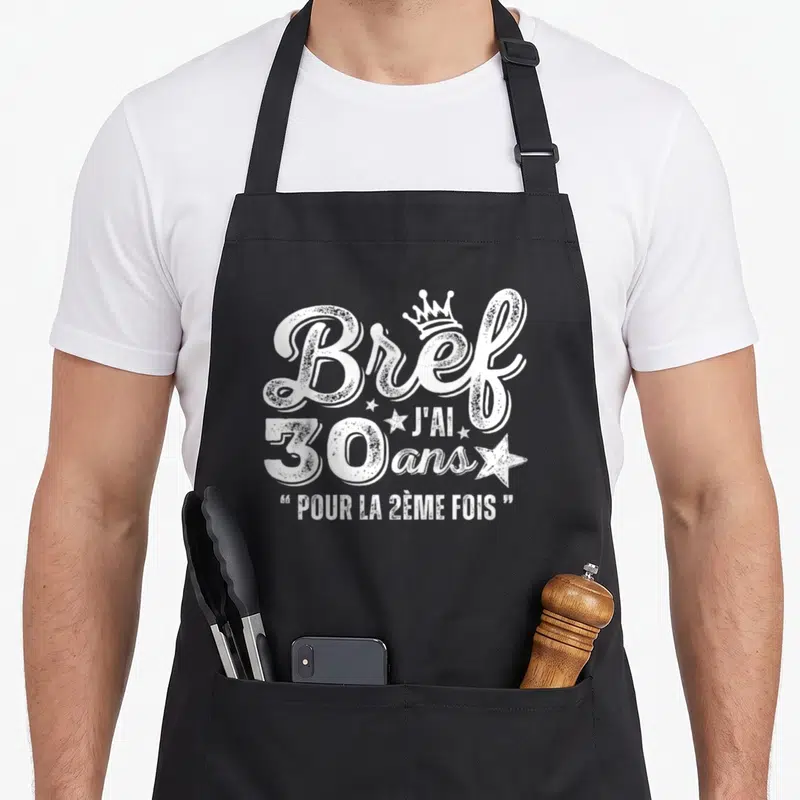 Tablier de cuisine noir avec l'inscription blanche Brief j'ai 30 ans pour la 2ème fois et une petite couronne.