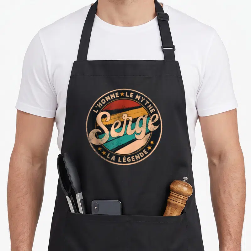 Tablier de cuisine noir avec logo circulaire rétro affichant le prénom Serge en lettres capitales stylisées.