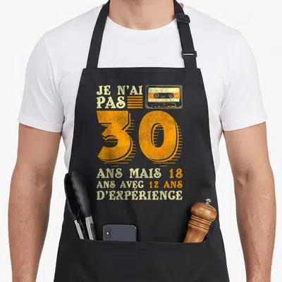 Tablier de cuisine noir avec une cassette orange, le chiffre 30 et un texte humoristique sur l'âge.