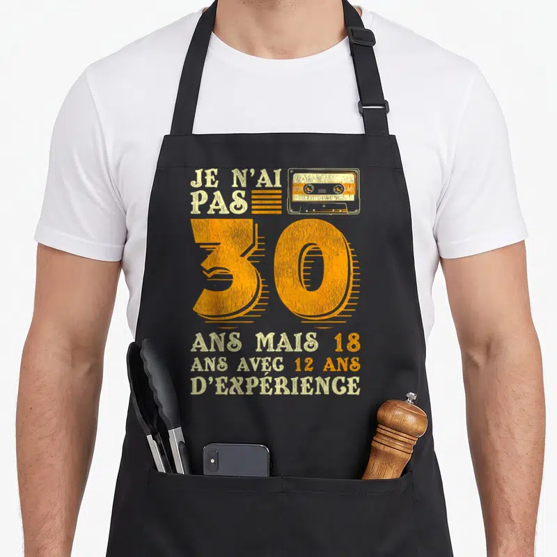 Tablier de cuisine noir avec une cassette orange, le chiffre 30 et un texte humoristique sur l'âge.