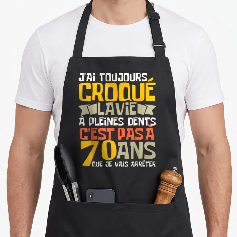 Tablier de cuisine noir avec inscription colorée J'ai toujours croqué la vie à pleines dents c'est pas à 70 ans que je vais arrêter.