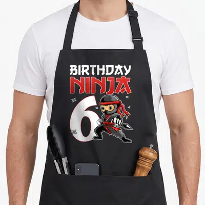 Tablier de cuisine noir avec illustration anniversaire Ninja 6 ans et shurikens rouges et blancs.