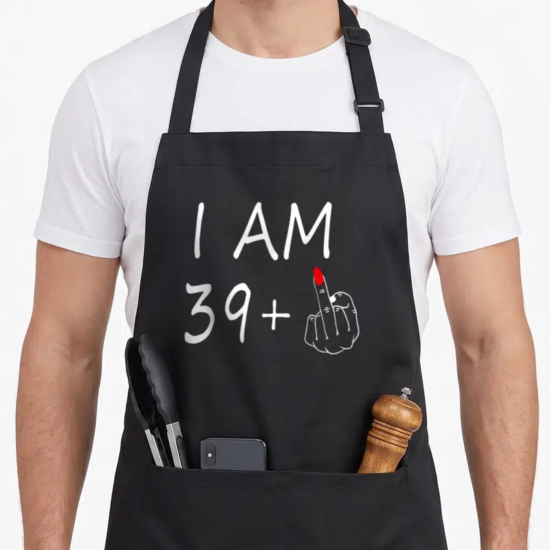 Tablier de cuisine noir avec inscription blanche I am 39 plus un majeur et une main levée au majeur à l'ongle rouge.