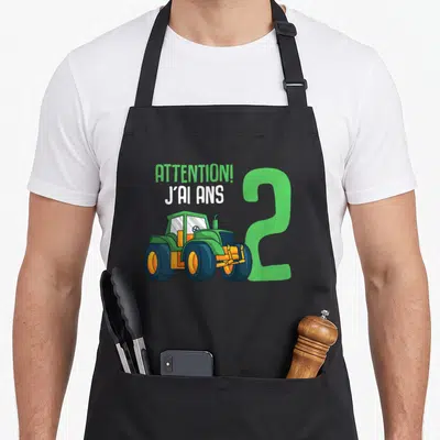 Tablier de cuisine noir avec illustration de tracteur vert et texte Attention j'ai 2 ans.